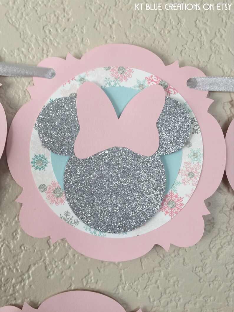 May include: Pink and silver glitter Minnie Mouse themed banner with snowflakes and a light blue background. The banner is made of cardstock and is perfect for a winter birthday party.