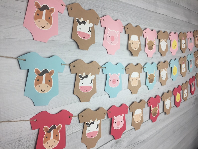 May include: A farm animal themed baby shower banner with alternating colors of pink, blue, and red. Each banner piece is shaped like a onesie with a different farm animal face on each. The animals include a horse, cow, pig, sheep, and a chick.