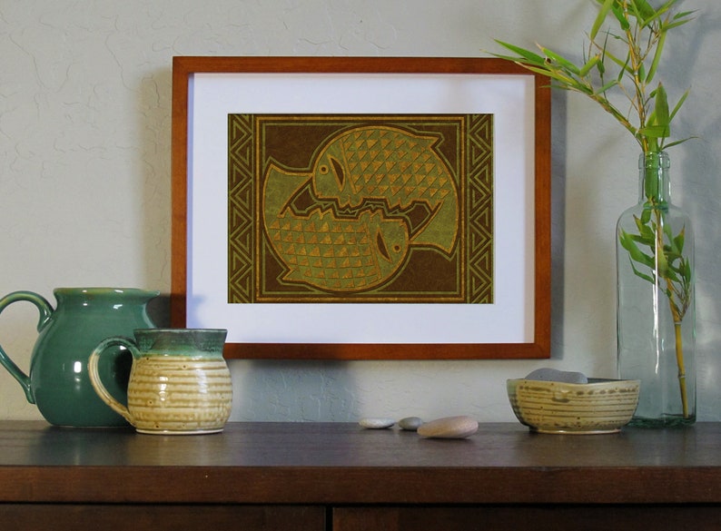 May include: A framed print of two stylized fish in a brown and green color scheme. The fish are facing each other and are surrounded by a geometric pattern.