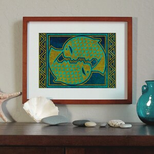 May include: A framed print of two stylized fish in gold and teal colors on a blue background. The fish are surrounded by a geometric border.
