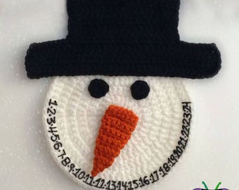 May include: White crocheted snowman face with black eyes, orange nose, and black numbers around the edge. The snowman is wearing a black crocheted hat.
