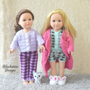 May include: Two dolls wearing crocheted pajamas and robes. One doll is wearing a purple and black plaid pajama set with a lavender cardigan. The other doll is wearing a blue and black plaid pajama set with a pink robe. A small stuffed husky dog is sitting in front of the dolls.
