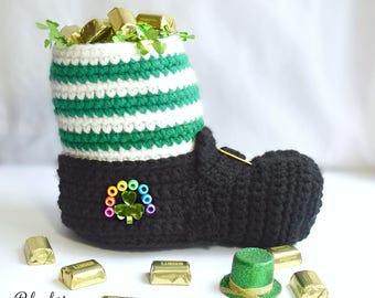 May include: A handcrafted crochet leprechaun boot in black, white, and green, filled with gold-wrapped candies and green sprigs. The boot features a shamrock embellishment and a small green top hat. The text "Blackstone Designs" is visible.