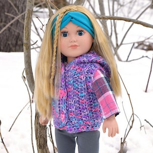 May include: A doll wearing a purple and pink crocheted vest with a plaid shirt underneath, grey trousers, and pink boots. The doll has blonde hair with a braid and is wearing a turquoise headband. The doll is standing in front of a snowy background.