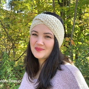 May include: A woman wearing a white crocheted headband with a criss-cross design. The headband is worn over her forehead and covers her ears. She is wearing a light purple sweater.