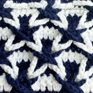May include: Close-up of a crocheted fabric with a repeating pattern of white and navy blue stars. The fabric is made with a textured stitch that creates a three-dimensional effect.