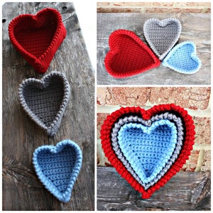 May include: Three crocheted heart-shaped baskets, one red, one gray, and one blue. The baskets are nested inside each other, with the largest basket on the bottom and the smallest basket on top.