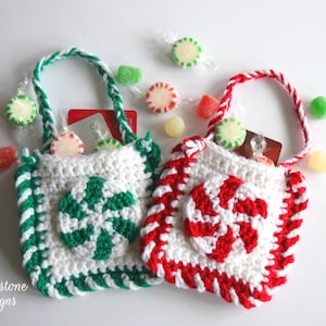 May include: Two small crocheted gift bags with candy cane designs. One bag is red and white, the other is green and white. Both bags have white handles and are filled with candy.