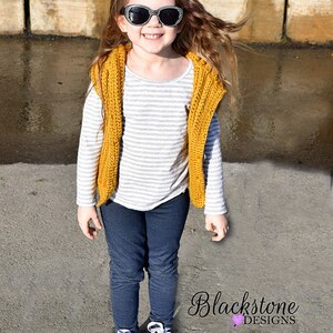 May include: A young person wearing a yellow crocheted vest over a striped shirt, blue jeans, and black and white sneakers. The person is wearing black sunglasses and has long brown hair.