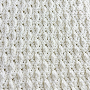 May include: Close-up of a white crocheted fabric with a textured, woven pattern. The fabric has a subtle sheen and a soft, airy feel.