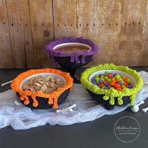 Puede incluir: Tres cuencos de ganchillo negros con interiores blancos, cada uno lleno de diferentes artículos. Uno tiene un borde naranja y cereales, otro tiene un borde verde y caramelos, y el tercero tiene un borde morado y un líquido marrón.
