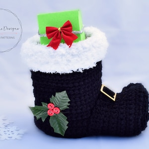 May include: Black crochet boot with a white fur cuff, filled with a green gift box with a red bow. The boot has a gold buckle and a green holly sprig with red berries.