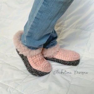 May include: Pink and gray crochet slippers with faux fur trim. The slippers have a gray sole and a pink upper with a fluffy, light pink trim around the ankle. The text "Blackstone Designs" is visible in the lower right corner.