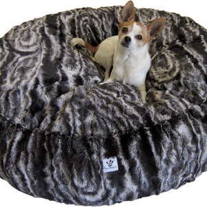 Könnte beinhalten: Ein rundes, grau-weißes Kunstfell-Hundebett mit einem kleinen Hund, der in der Mitte sitzt. Das Bett hat ein Wirbelmuster und der Hund schaut in die Kamera.