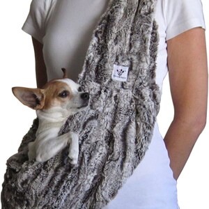 Könnte beinhalten: Eine graue Haustier-Tragetasche aus Kunstfell mit einem kleinen Hund darin. Die Tasche wird über der Schulter getragen und hat ein Etikett mit der Aufschrift "Revive & Peace". Der Hund ist weiß und braun.
