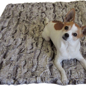 K&ouml;nnte beinhalten: Ein kleiner, wei&szlig;er und brauner Hund mit braunen Augen liegt auf einem grauen und braunen Kunstfell-Hundebett.