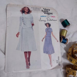 May include: A vintage sewing pattern from Very Easy Vogue, featuring a design by Jerry Silverman. The pattern includes illustrations of a two-piece outfit. Spools of thread in green, yellow, and blue, along with a measuring tape, are also visible.