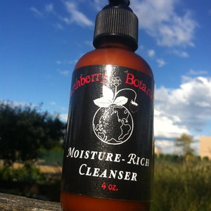 K&ouml;nnte beinhalten: Eine braune Flasche mit schwarzem Pumpspender und schwarzem Etikett. Das Etikett tr&auml;gt einen wei&szlig;en Text mit der Aufschrift "Earthberry Botanics Moisture-Rich Cleanser 4 oz.".