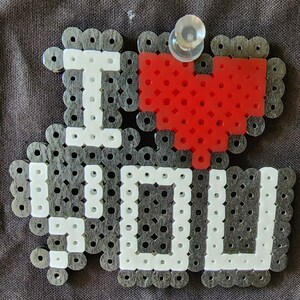 Puede incluir: Un dise&ntilde;o de cuentas negras y blancas que dice "Te amo" con un coraz&oacute;n rojo en el centro.