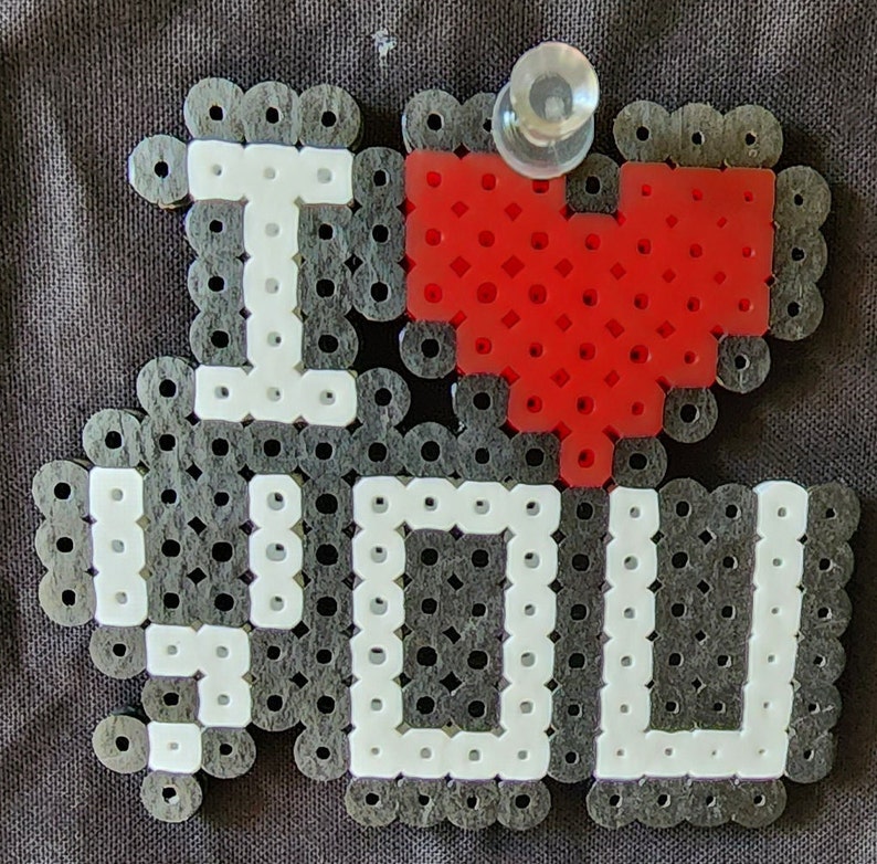 Puede incluir: Un dise&ntilde;o de cuentas negras y blancas que dice "Te amo" con un coraz&oacute;n rojo en el centro.