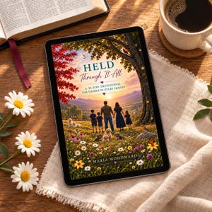 以下が含まれることがあります： マリア・ウッドワード著の31日間のデボーションブック「Held Through It All」の表紙を表示したデジタルタブレット。表紙には、夕暮れ時の野花が咲き乱れる草原に立つ家族と、その周りに木々、鳥、小さな犬たちが描かれています。