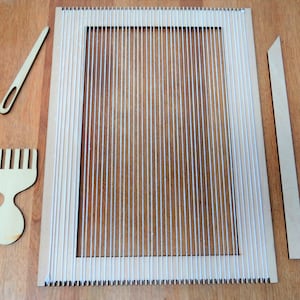 May include: A wooden loom with white string warp threads, a wooden comb, a wooden needle, and a wooden dowel. The loom is on a wooden surface.