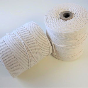 May include: Two spools of white cotton twine. The twine is wound tightly around the spools, which are made of cardboard.