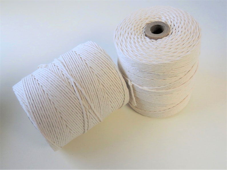 May include: Two spools of white cotton twine. The twine is wound tightly around the spools, which are made of cardboard.