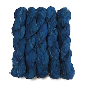May include: Five skeins of deep blue silk ribbon yarn arranged side by side. Each skein features a crinkled, textured surface with frayed edges and a consistent dark indigo colour throughout the entire length of the fabric strips.