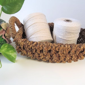 May include: Two spools of white cotton twine in a brown wicker basket. The basket has a woven design and two handles.