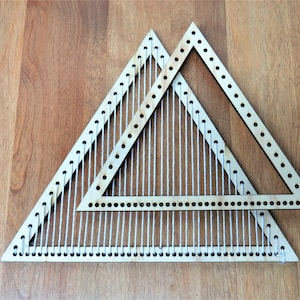 Könnte beinhalten: Zwei dreieckige Webrahmen aus Holz, wobei einer in den anderen eingebettet ist. Die Webrahmen sind aus hellbraunem Holz gefertigt und haben einen weißen Faden, der durch die Löcher gewebt ist.