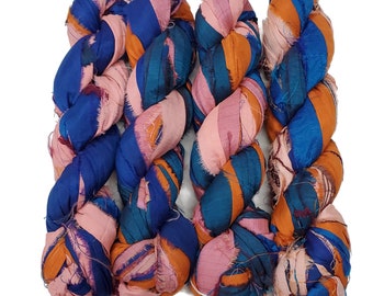 May include: Three skeins of colorful silk ribbon, twisted together. The ribbon is a mix of blue, orange, and pink.