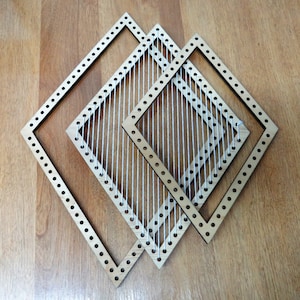 以下が含まれることがあります： 白い糸が穴に通された、木製の正方形の織り枠が3つあります。枠は互いに重ねられており、層状の効果を生み出しています。