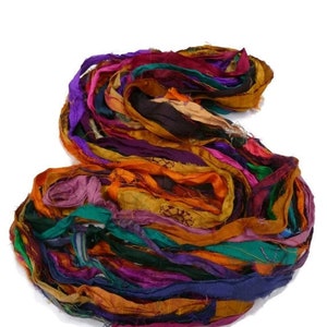 May include: A bundle of colorful silk ribbon scraps in shades of purple, orange, green, and brown. The ribbon is perfect for crafting and adding a touch of whimsy to projects.