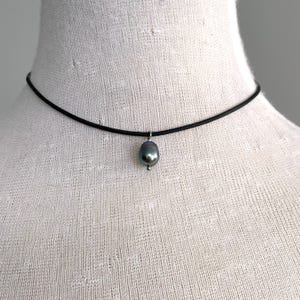 Puede incluir: Un collar choker negro simple con un colgante de perla gris oscuro.