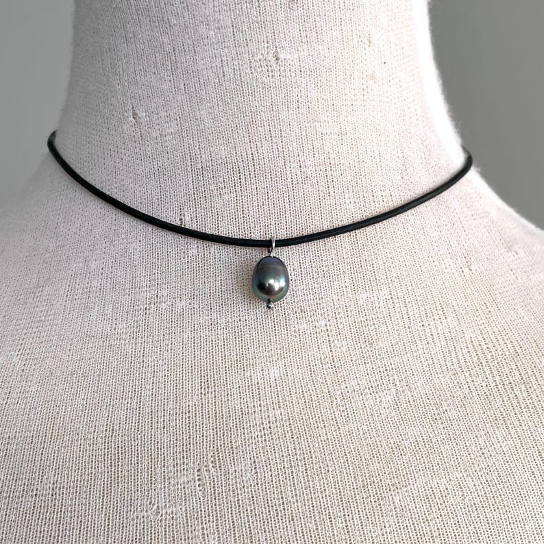 Puede incluir: Un collar choker negro simple con un colgante de perla gris oscuro.