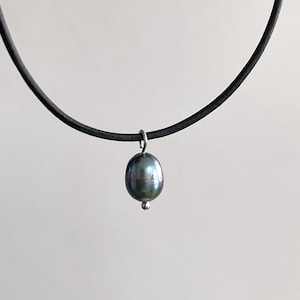 Puede incluir: Un collar gargantilla de cuero negro con un colgante de perla gris oscuro.