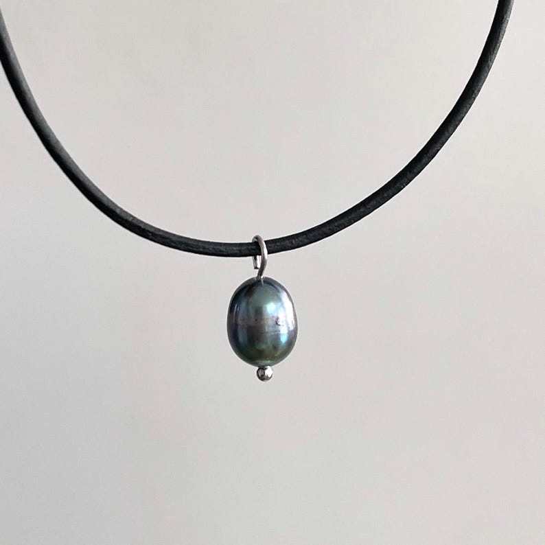 Puede incluir: Un collar gargantilla de cuero negro con un colgante de perla gris oscuro.