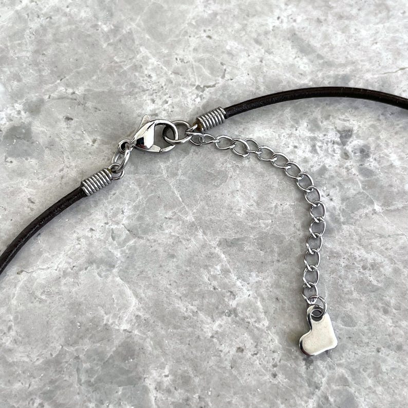 Puede incluir: Un collar de cord&oacute;n de cuero marr&oacute;n con un cierre plateado y un dije de coraz&oacute;n plateado en una cadena extensora.