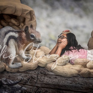 May include: A young girl wearing a pink shirt and a headband lies on a bed of peanuts, looking at a chipmunk sitting on a pile of peanuts. The peanuts are spilling out of a large brown sack.