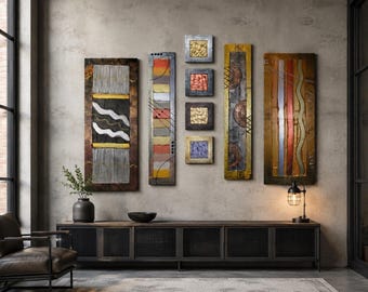 May include: A collection of seven wall art pieces featuring a mix of vertical rectangular and square panels. The artwork displays textured surfaces with metallic finishes in gold, copper, silver, and bronze, accented by geometric lines and patterns.