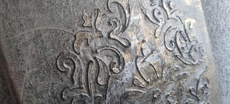 May include: A close-up of a textured, gray surface with a gold metallic design. The design features intricate swirls and flourishes.