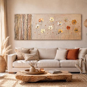 Könnte beinhalten: Ein großes, rechteckiges Leinwandkunstwerk mit einem Blumendesign mit goldenen und orangefarbenen Blumen. Das Kunstwerk hängt über einem cremefarbenen Sofa mit dekorativen Kissen und einer Fransen-Decke. Der Raum hat eine neutrale Farbpalette.
