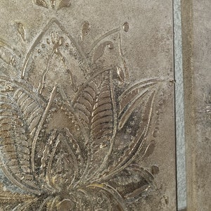 Op de afbeelding: Twee vierkante canvasdoeken met een reli&euml;fdesign. Het linker canvas heeft een zilverkleurig lotusbloemdesign. Het rechter canvas heeft een zilverkleurig bloemendesign.