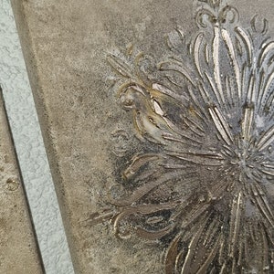 Op de afbeelding: Twee vierkante wanddecoraties van beige canvas met een reli&euml;f, gouden bloemmotief.