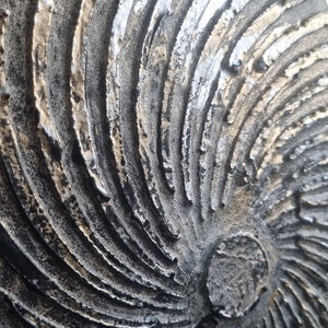 May include: A close-up of a textured, circular wall art piece with a swirling pattern in shades of gold, silver, and black.