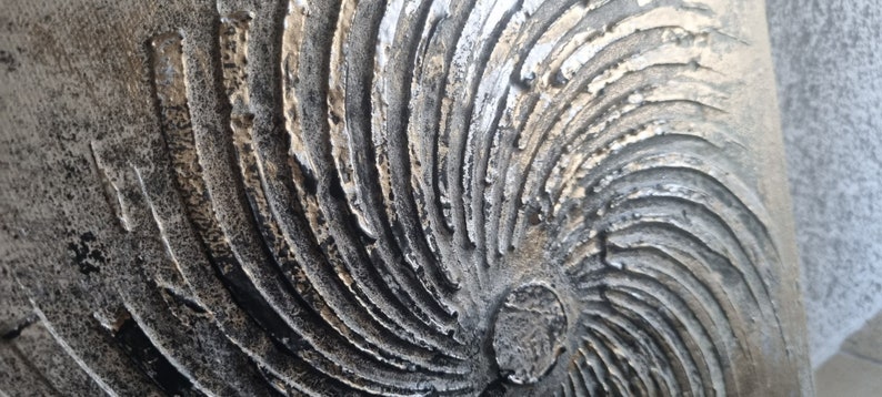 May include: A close-up of a textured, circular wall art piece with a swirling pattern in shades of gold, silver, and black.