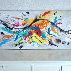 Può includere: Dipinto astratto su tela con sfondo bianco e schizzi di colore in tonalità di blu, verde, giallo, arancione, rosso e rosa. Il dipinto ha una linea nera che attraversa il centro.