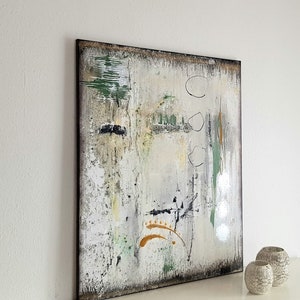 May include: Abstract art piece on a white wall. The artwork features a textured, multi-colored design with green, black, and gold accents. The painting is framed in a dark brown border. Two decorative vases sit on a white surface.