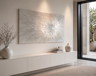 May include: A large, abstract artwork with a textured, silver-and-white burst design hangs above a white cabinet. A vase with branches and two other decorative vases sit on the cabinet. A window with a view of a tree is on the right.